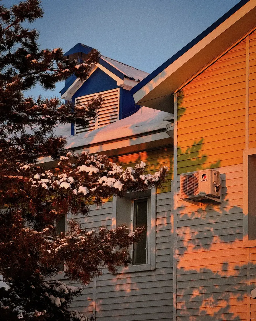 Two-storey house with warm light on the siding at dusk among bare trees