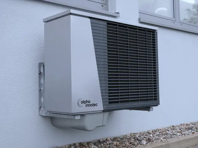 Outdoor heat pump unit mounted on a pale wall of a house