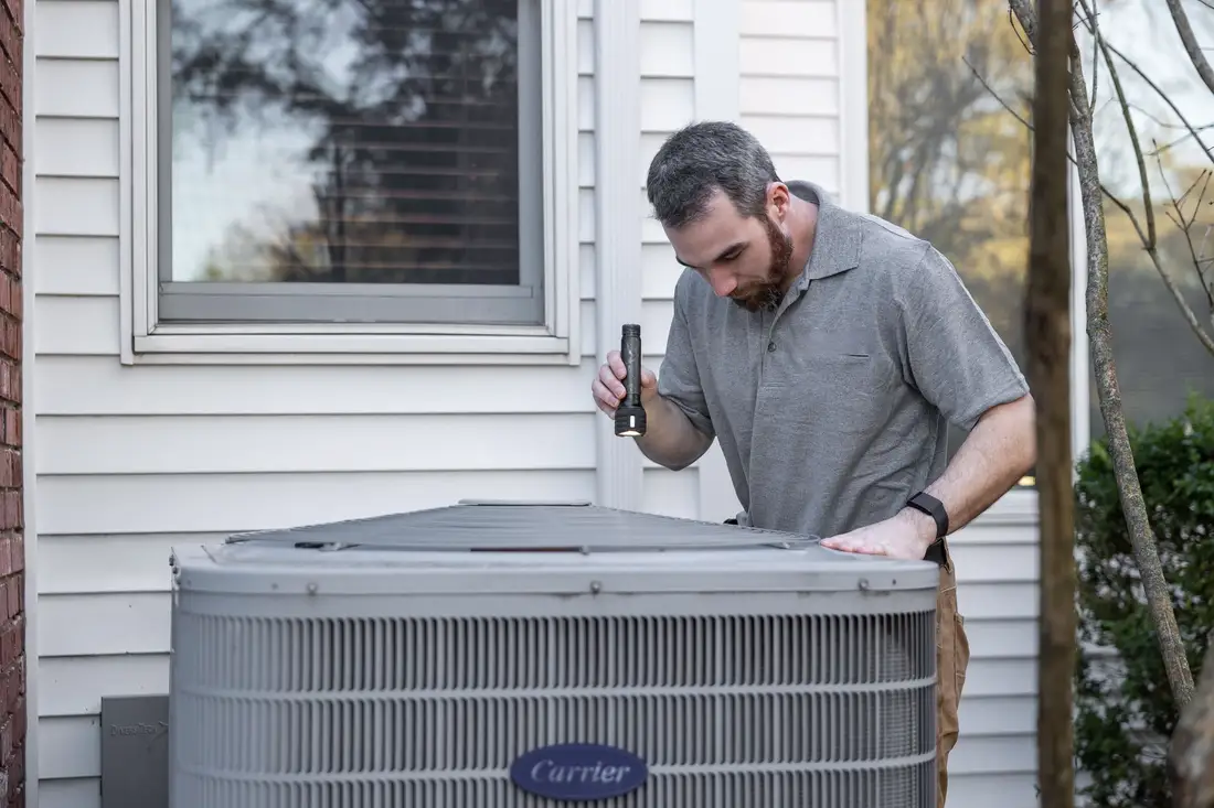 Technician working on an outdoor heat pump unit next to a house